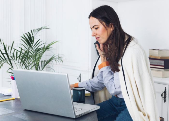 Une femme avec un plaid sur les épaules travaille sur son ordinateur tout en téléphonant avec son portable.