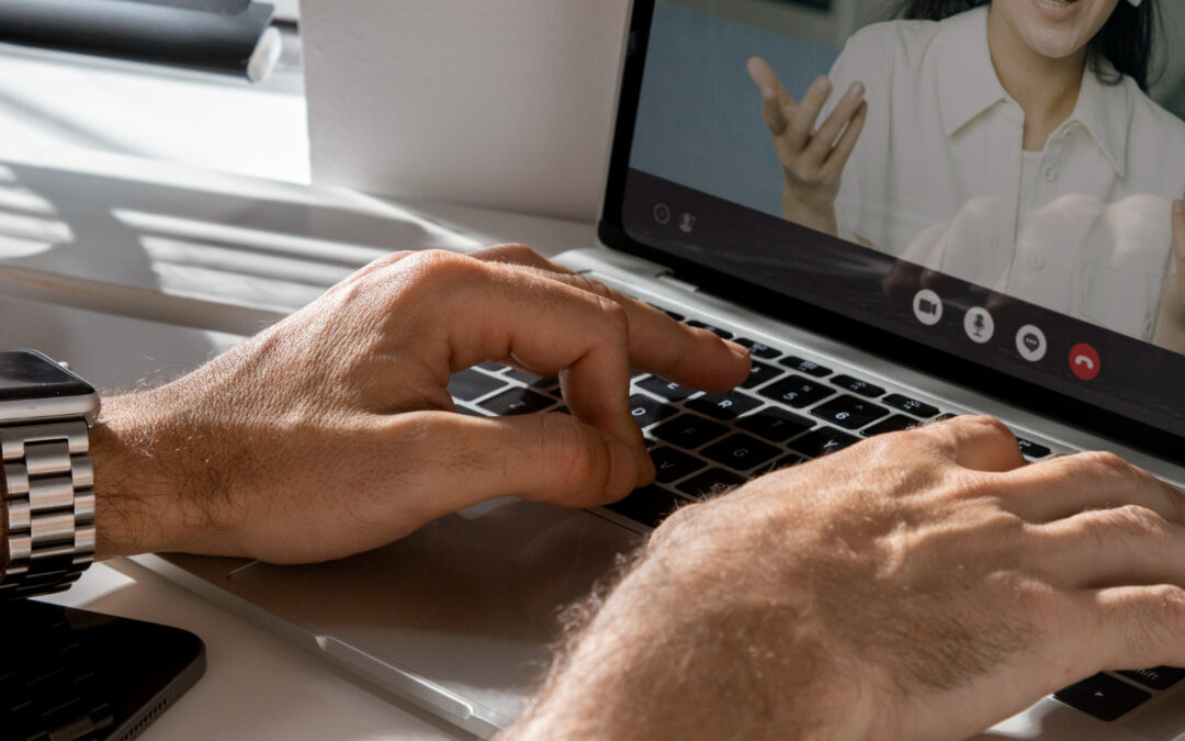 les mains d'un utilisateur tapant sur le clavier d'un ordinateur portable lors d'une visioconférence avec une interlocutrice affichée à l'écran