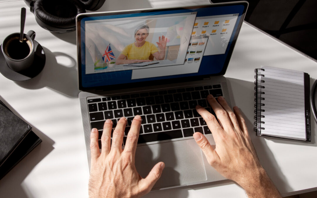 mains tapant au clavier d'un ordinateur portable ouvert sur une visioconférence, à côté d'une tasse de café et d'un carnet